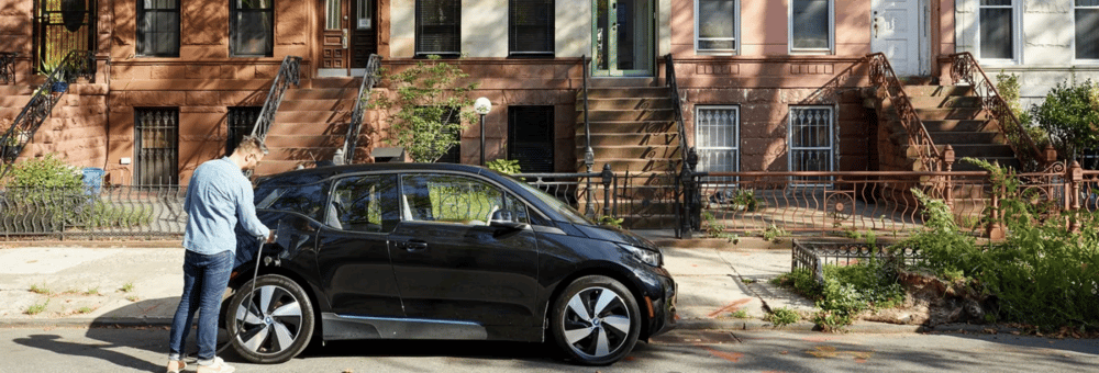 man charging electric car in front of apartment buildings Drive green EV
